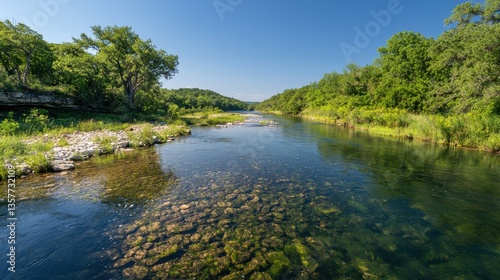 A serene river flows through lush greenery under a clear blue sky, showcasing a tranquil natural landscape.