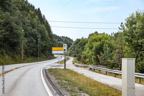 A road with a yellow sign and a camera on the side in Norway