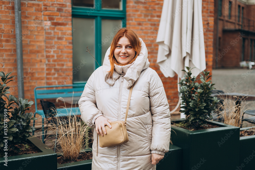 Stylish attractive young smiling 30s woman walking on city street in winter outfit, old town. Urban lifestyle concept. Portrait of happy woman looking at camera outdoor. High quality photo.