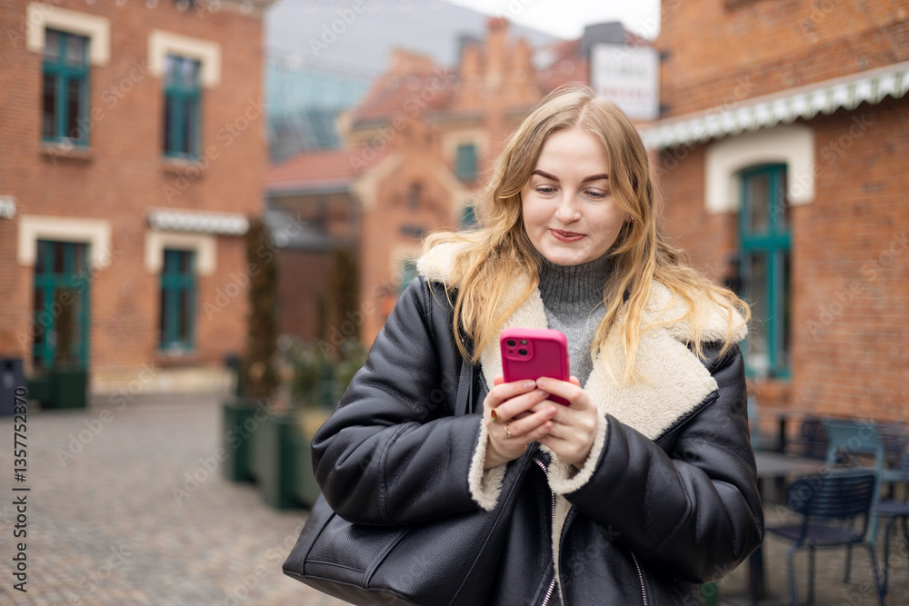 Young stylish 30s woman writes message on smartphone walking on city street. Urban lifestyle concept. Autumn time. Charming female wearing stylish outfit chatting online. High quality photo.