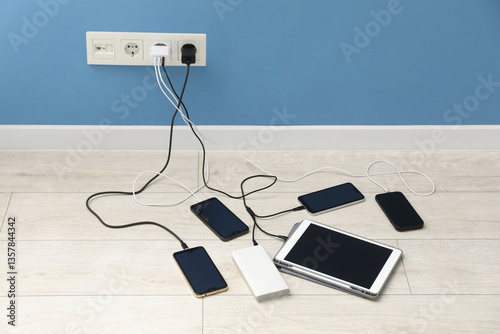 USB adapters with cables plugged into electric socket charging different devices indoors