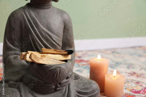 Buddha statue with palo santo sticks and burning candles indoors, closeup. Space for text