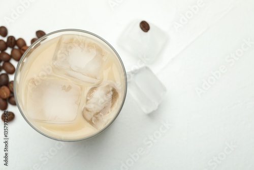 Coffee cream liqueur in glass, ice and beans on white table, flat lay. Space for text