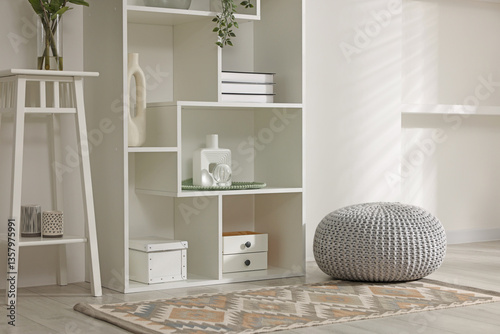Shelving unit with decor, stool and pouf near white wall indoors