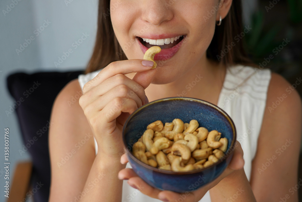 Cashew nuts. Unidentified young woman eating cashew nuts as snack at home.
