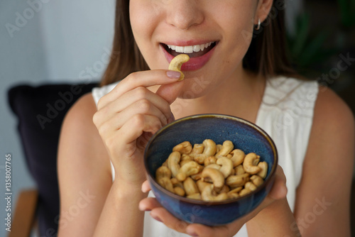Obraz na płótnie Cashew nuts. Unidentified young woman eating cashew nuts as snack at home. w salonie