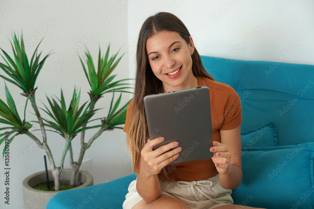 Portrait of Hispanic young woman using tablet sitting on couch in her apartment