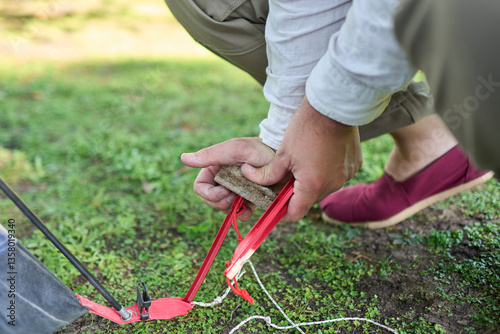 Unknown person using a stone as a hammer to drive a tent peg into the ground.