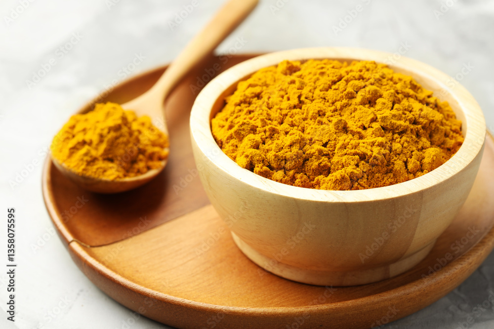 Turmeric powder in bowl and spoon on light grey table, closeup Turmeric powder in bowl and spoon on light grey table, closeup