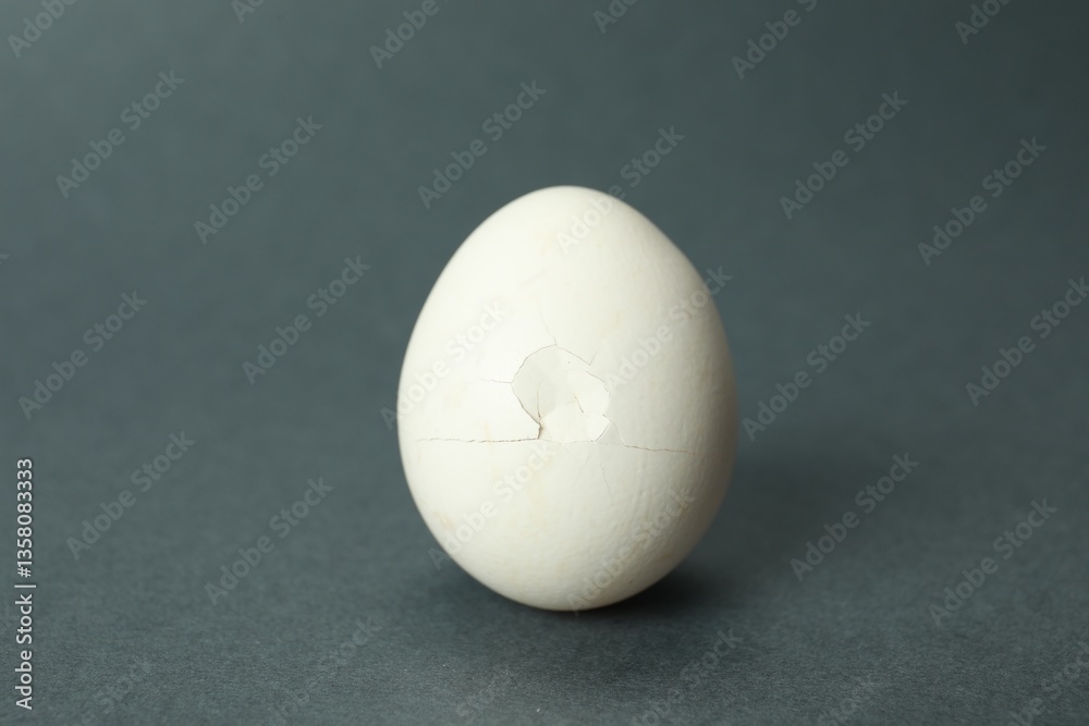 One egg with cracked shell on grey background, closeup One egg with cracked shell on grey background, closeup