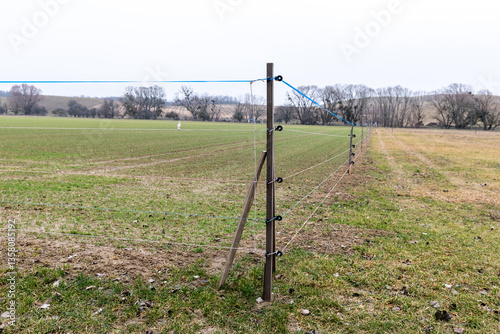 Electric fence wire running along a fence in the middle of a field.