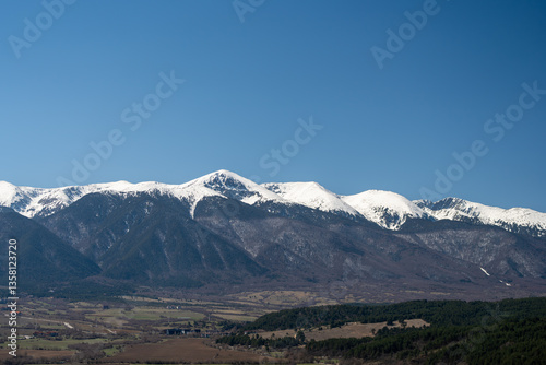 Snow capped mountain range towering over rural landscape under blue sky