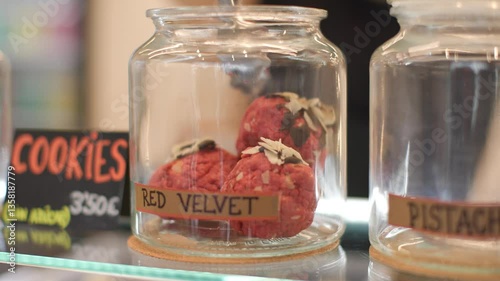 Close-up shot of a chef placing red velvet cookies into a labeled glass jar for display at a take-away food shop. Cozy small business concept with artisanal presentation.