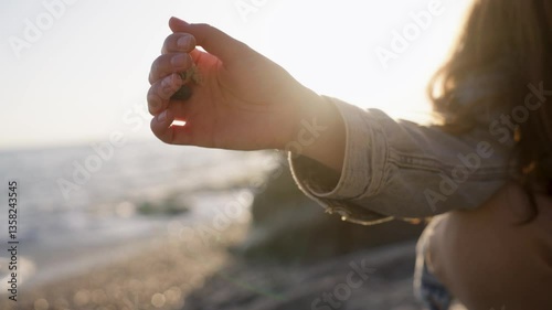 A hand gently releasing small pebbles on the beach, illuminated by the warm golden light of sunset. A moment of tranquility, symbolizing the passage of time and letting go