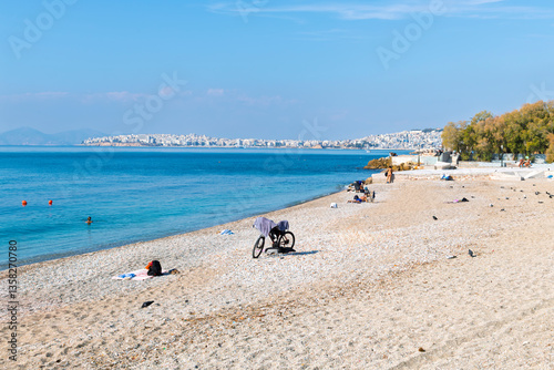 A sandy pebble beach along the Aegean Sea at the  promenade of Flisvos along the Athenian Riviera with Piraeus city behind, in Palaio Faliro, Greece.	