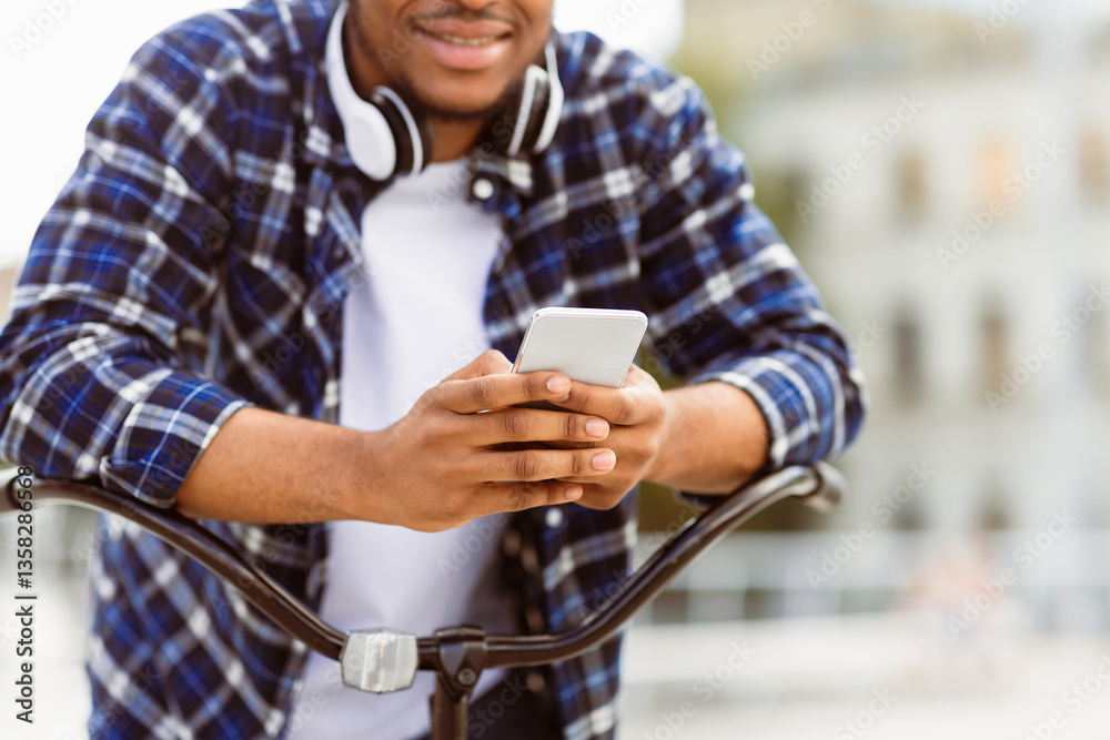 Technology And Communication Concept. Unrecognizable afro man using his cell phone, leaning on bike Technology And Communication Concept. Unrecognizable afro man using his cell phone, leaning on bike