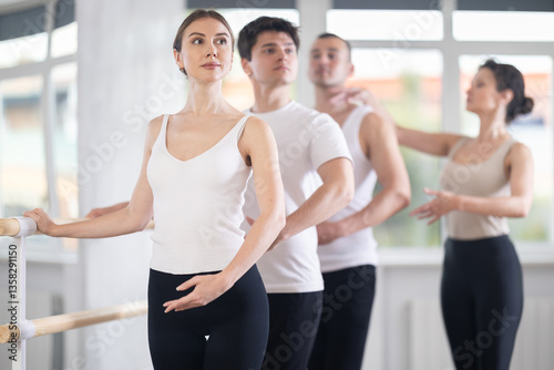 Experience female ballet instructor adjusting students form. Diligent girls and boys practice ballet movements near ballet barre in modern dancing hall