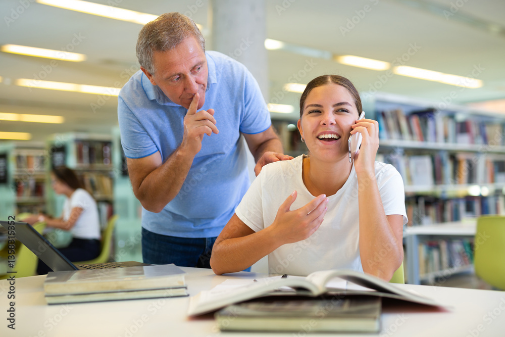 Obraz premium Elderly librarian asks young woman who is talking loudly on a mobile phone to keep quiet