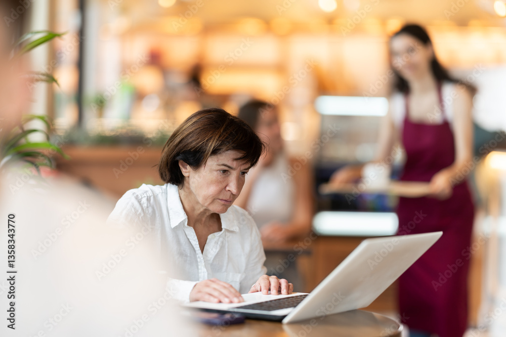 © JackF - Mature woman sitting at a table in a coffee shop and working attentively on her laptop. European pensioner is working on a laptop in a cafe © JackF - Mature woman sitting at a table in a coffee shop and working attentively on her laptop. European pensioner is working on a laptop in a cafe