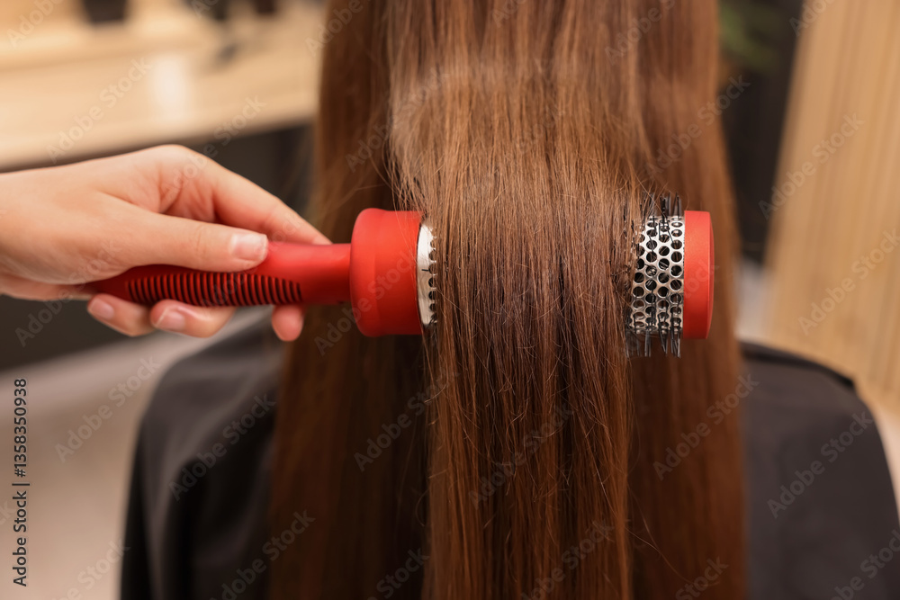 Fototapeta premium Hairdresser styling client's hair with round brush in salon, closeup