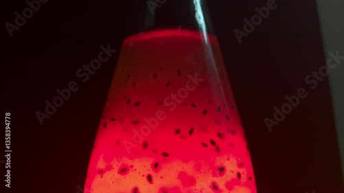 Top of the bottle. Liquid glowing bright red in a transparent bottle. On a dark black background, with a glare. Air bubbles rise up. Bubbles in the middle of plant seeds. Drink with plant seeds glows.