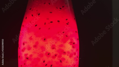 A bright red glowing liquid in a transparent bottle. On a dark black background. Air bubbles rise up. Bubbles In the middle of plant seeds. The drink with plant seeds glows