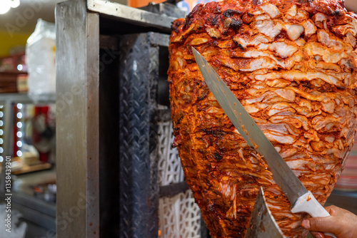 Mexican vendor preparing tacos al pastor, slicing meat from a vertical spit in a traditional taqueria