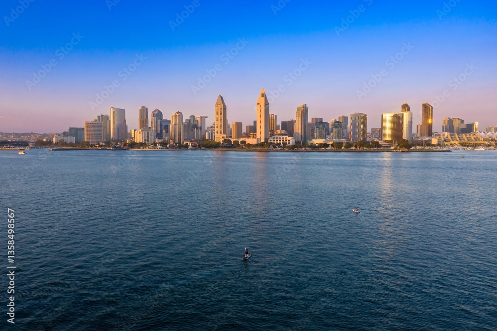 Obraz premium Paddleboarders enjoy the calm waters of San Diego Bay, USA, with the city skyline in the background. Recreation and urban landscape blend in this scenic view.