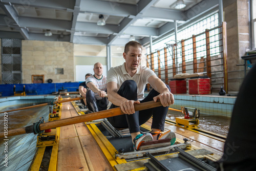 Exhausted determined rowers push limits training intensely on rowing simulator in gym pool. Male crew muscle endurance, synchronized strokes, breath control, power output, stamina strength challenge photo