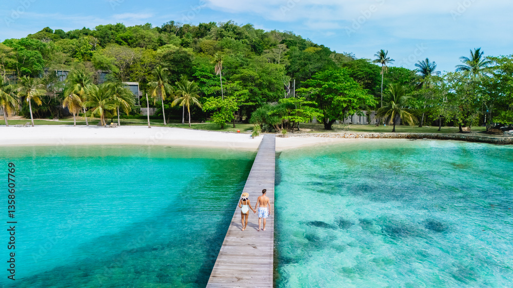 A couple enjoys a serene walk along a wooden pier on Koh Kham Island in Thailand. The turquoise waters and palm trees create a blissful tropical atmosphere perfect for relaxation. A couple enjoys a serene walk along a wooden pier on Koh Kham Island in Thailand. The turquoise waters and palm trees create a blissful tropical atmosphere perfect for relaxation.