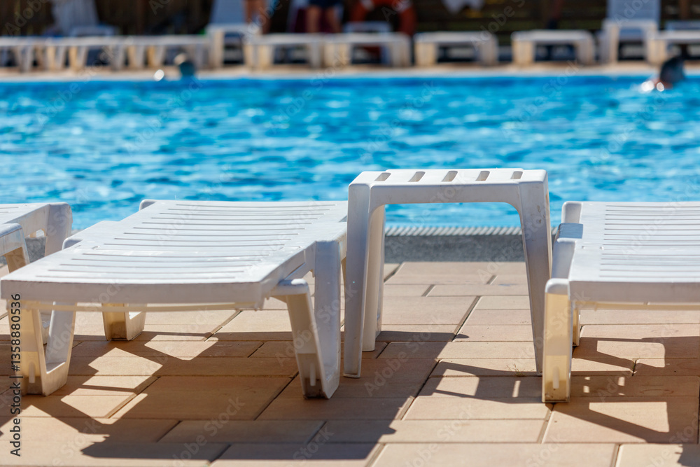 A row of white lounge chairs are set up on a patio next to a pool A row of white lounge chairs are set up on a patio next to a pool
