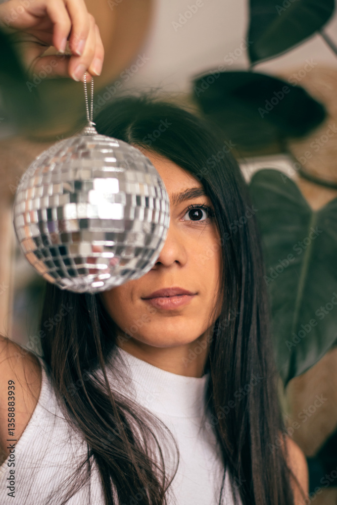Portrait of a young dark-haired woman covering half of her face with a disco ball.Home decor.