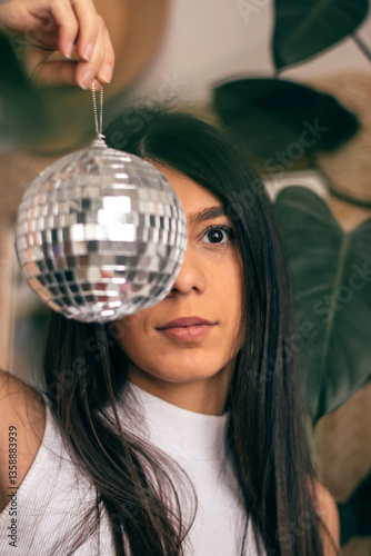 Obraz na płótnie Portrait of a young dark-haired woman covering half of her face with a disco ball.Home decor. w salonie