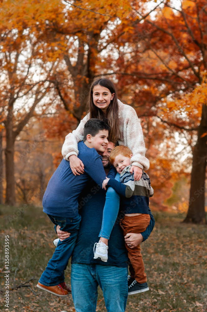 Strong dad holds up 3 of his kid at once at pretty park on autumn day