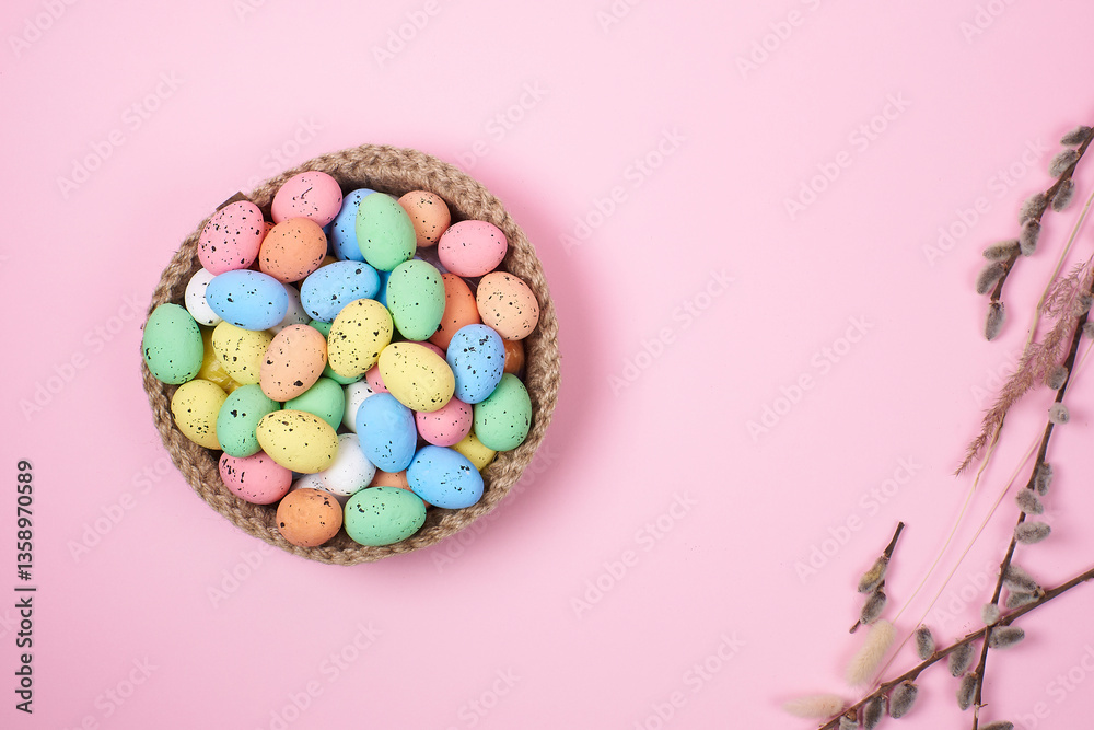 Obraz premium Willow twigs with colorful Easter eggs in a plate on a pink background, top view