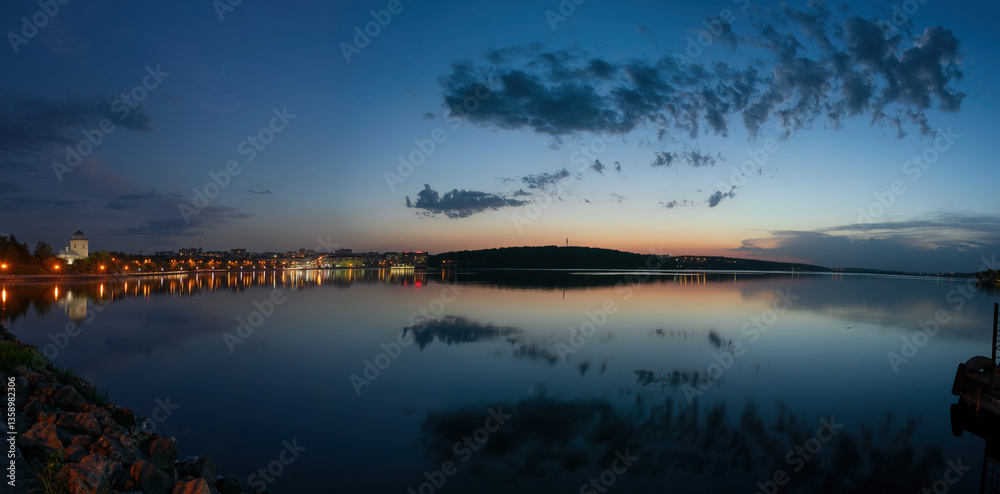 Fototapeta premium Panoramic view of City Pond reflecting the lights of Ternopil and the colorful sunset sky in Ukraine, creating a peaceful and scenic atmosphere