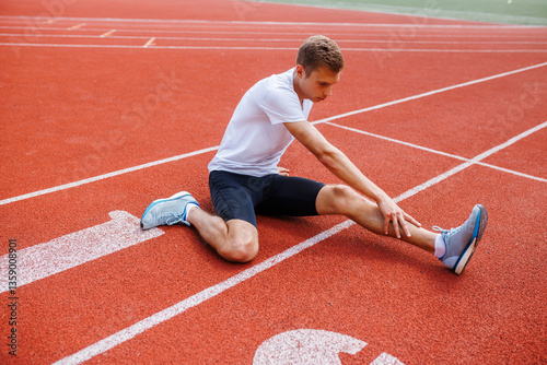 Fototapeta Naklejka Na Ścianę i Meble -  Athlete stretching on a running track, preparing for training or competition, focused on flexibility and injury prevention in sports