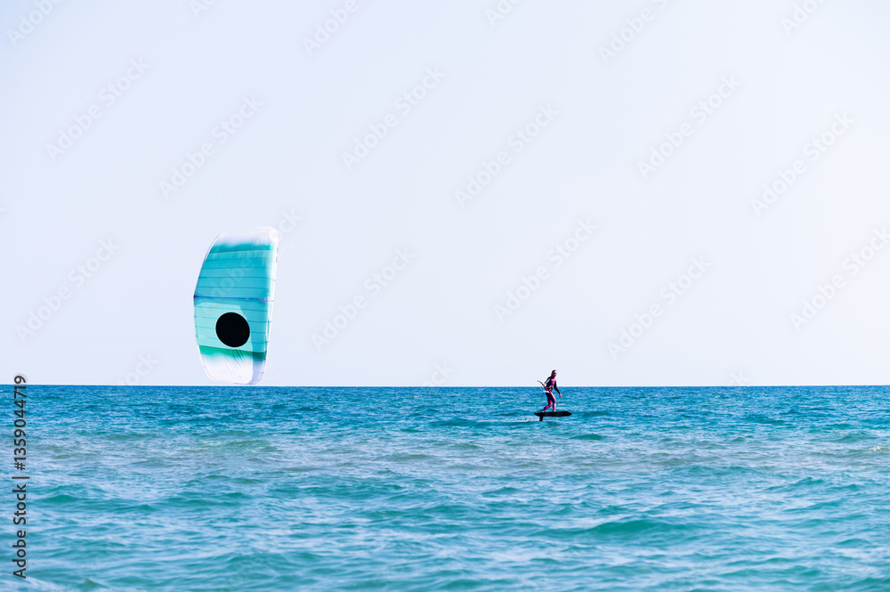 Naklejka premium woman at sea rides a hydrofoil surfboard using a kite wing. Extreme sport, fast travel across the sea on a board