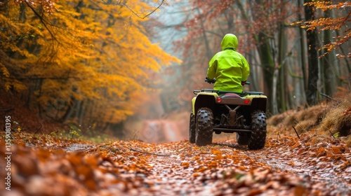 A person in a bright green jacket rides an ATV along a forest trail covered in vibrant autumn leaves. The yellow and orange foliage creates a picturesque backdrop, capturing the essence of fall