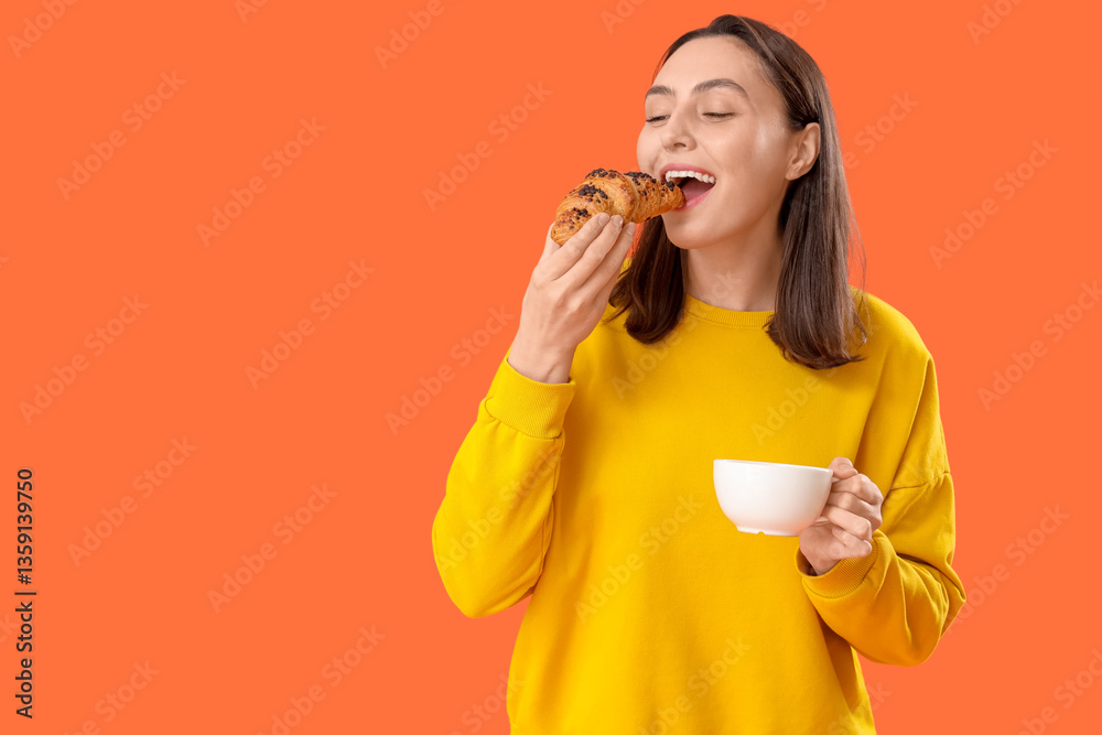 Young woman with cup of tea and tasty croissant on orange background Young woman with cup of tea and tasty croissant on orange background