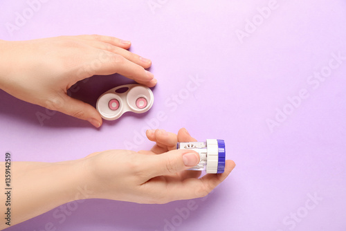 Female hands with cleaning case for contact lenses and container on lilac background