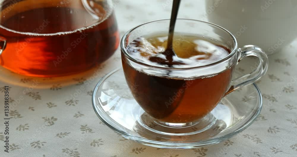 Adding and stirring sugar in cup with aromatic tea at table, closeup Adding and stirring sugar in cup with aromatic tea at table, closeup