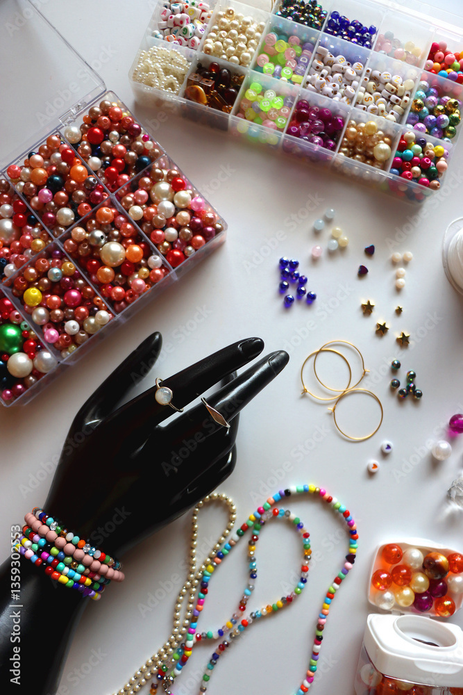 Hand figurine, colorful friendship bracelets, necklaces, various beads and DIY supplies on the table. Making jewelry at home. Flat lay.