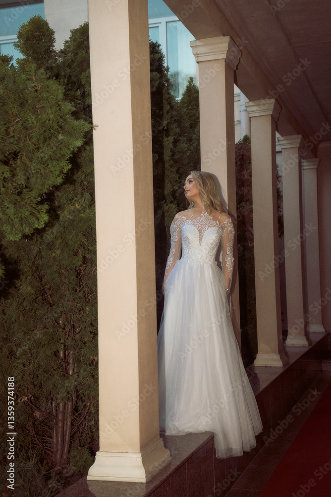 Fototapeta premium beautiful blonde bride posing in open gallery of hotel. in long wedding dress