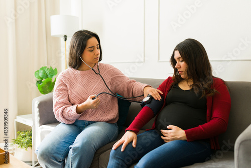 Female medical professional measuring blood pressure for expecting patient during home consultation, ensuring maternal health monitoring