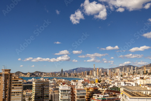 Obraz na płótnie Photo overlooking the old town of Benidorm in Spain showing the West Beach Promenade surrounded by high rise apartments and buildings with the mountains and white clouds in the background w salonie