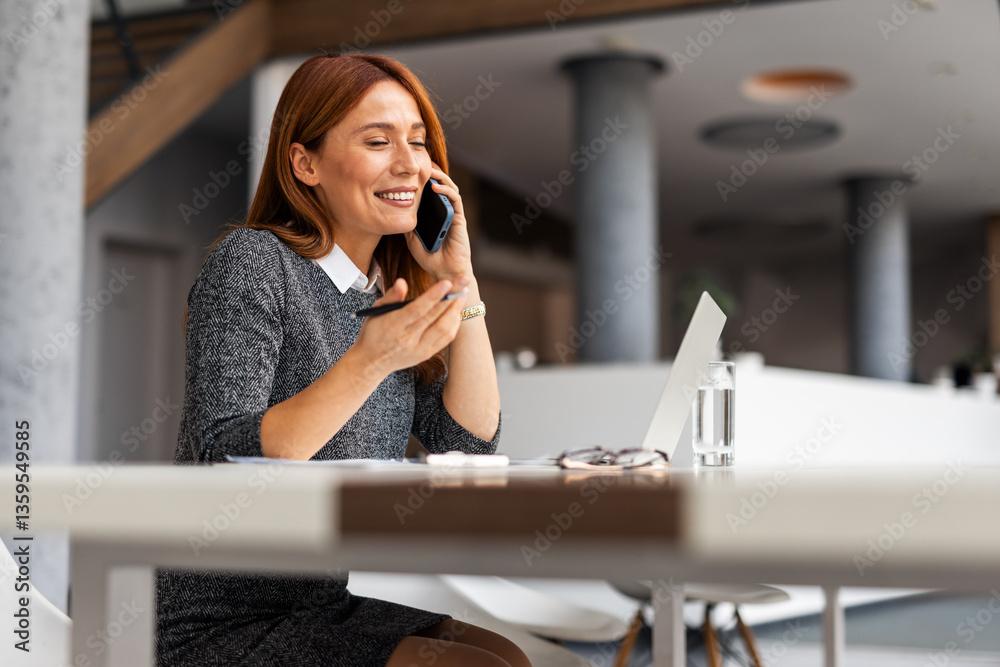 Professional Woman Talking on Phone While Working on a Laptop in Office