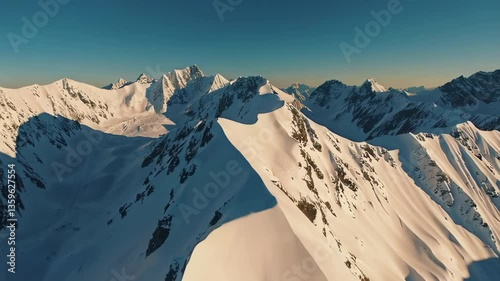 Aerial drone shot flying smoothly over majestic mountain range with snow-capped peaks and golden sunlight, showcasing breathtaking natural scenery for travel, landscape, and cinematic visuals