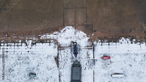 Aerial view capturing a car towing a boat on a trailer near the snowy Kauno Marios in Lithuania, highlighting winter boat storage and transportation in a serene, frozen landscape photo