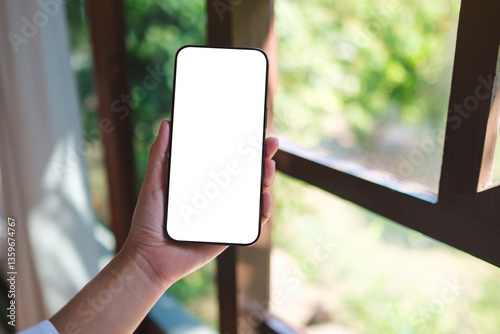 Mockup image of a woman holding mobile phone with blank desktop screen at home